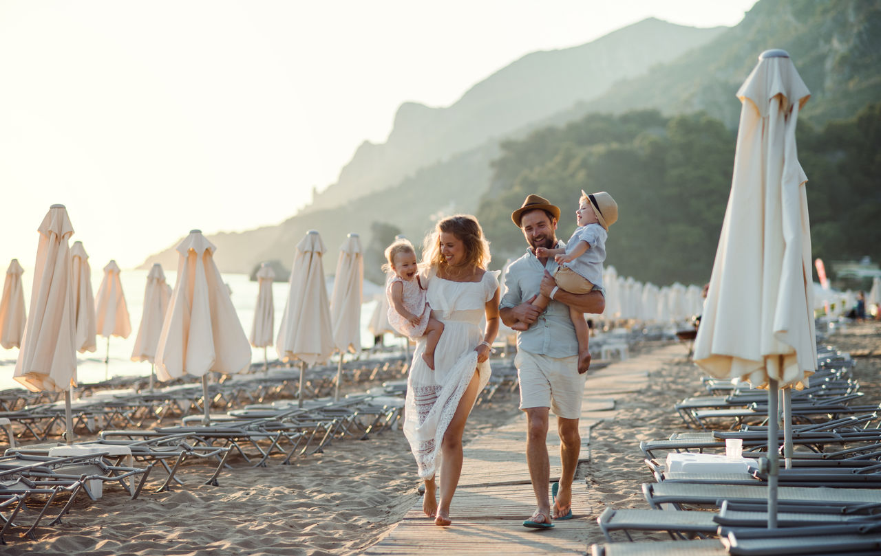 Junge Familie mit zwei Kleinkindern, die im Sommerurlaub am Strand spazieren gehen.